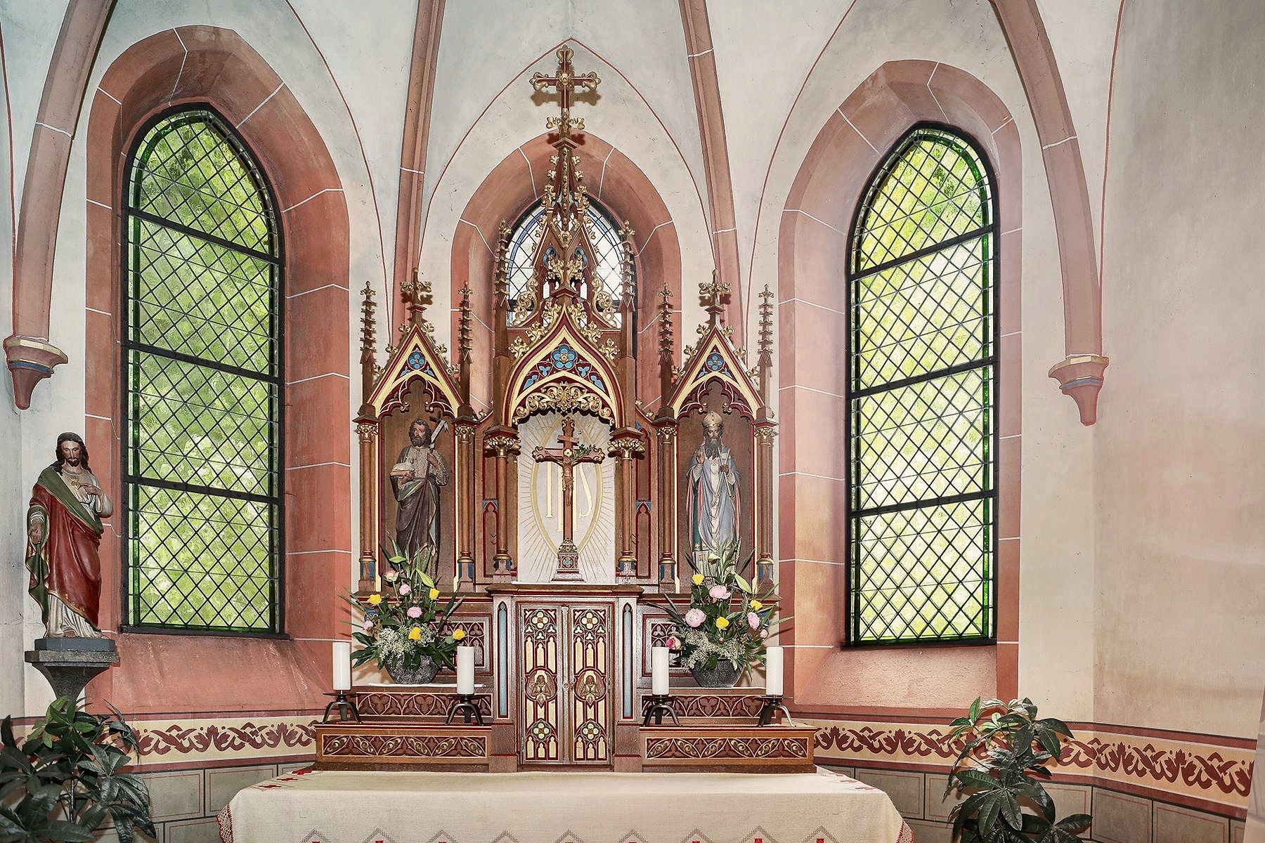 Der Chor mit Altaraufsatz, zwei Bleiglasfenstern und einer Figur links